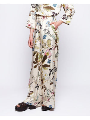 The woman showcases the MIRTO 1956 Botanical Floral Print Fluid Pants with an elastic waistband, complemented by a matching wide-brimmed hat and floral outfit, against a plain background.