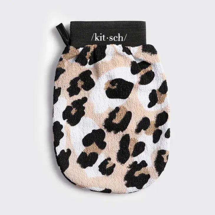 Image of a KITSCH ECO FRIENDLY EXFOLIATING GLOVE. It features a beige, black, and dark brown leopard print pattern. The eco-friendly packaging is beige with text indicating the body scrubber is designed for softening skin. The glove hangs on a peg against a plain backdrop.