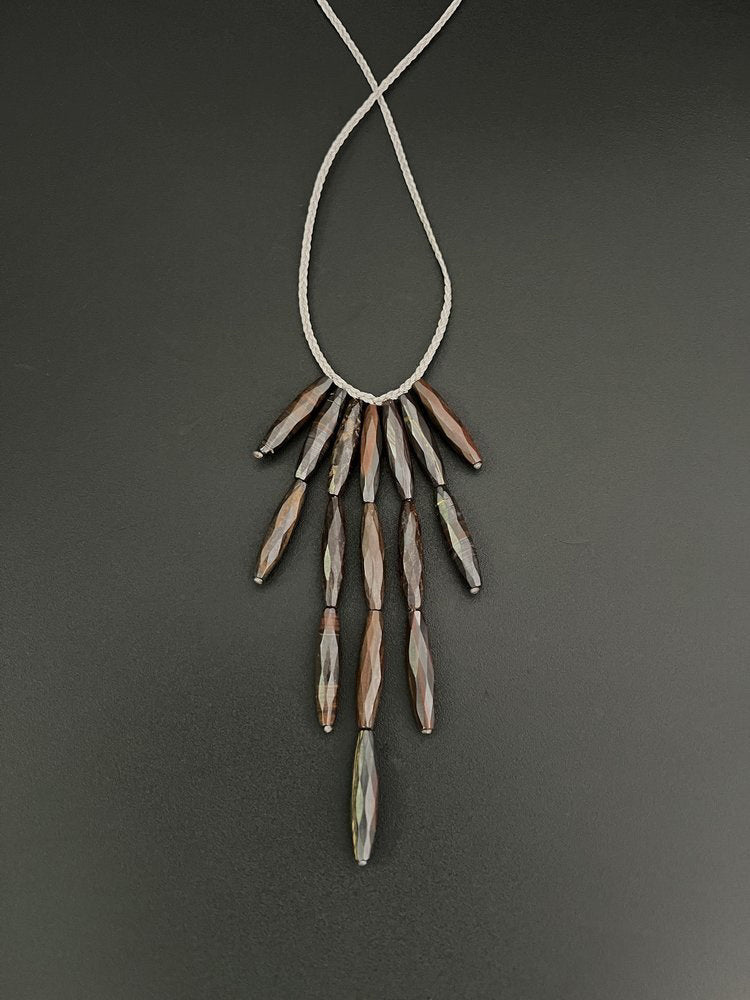 The ANN LIGHTFOOT - BRONZITE DEMI-FRINGE NECKLACE showcases elongated, faceted brown beads arranged in a cascading fringe design on a delicate grey cord. Lustrous bronzite droplets are elegantly displayed in two symmetrical tiers, and its adjustable ties guarantee an ideal fit for every wearer.