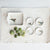 The BIRD CURIO DISH by CREATIVE COOP features a ceramic rectangular dish and four bowls with bird illustrations on parchment paper, complemented by a stoneware dish next to seven green tomatillos with husks for a rustic composition.