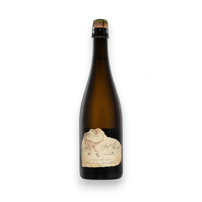 A tall brown glass bottle of RED TAIL RIDGE PERPETUAL CHANGE SPARKLING WINE by WINE: OCEAN SOUTH IMPORTS, made in Champenoise style with a cork. The cream label shows a frog and handwritten text, set against a white background.