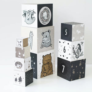 The WEE GALLERY - BABY ANIMAL NESTING BLOCKS, featuring monochrome animal illustrations and numbers, are perfect for developing early math concepts. The left stack includes woodland animals, while the right stack displays numbers 5, 6, and 7 adorned with more animal images. These nesting blocks from WEE GALLERY also help enhance motor skills against a plain white background.