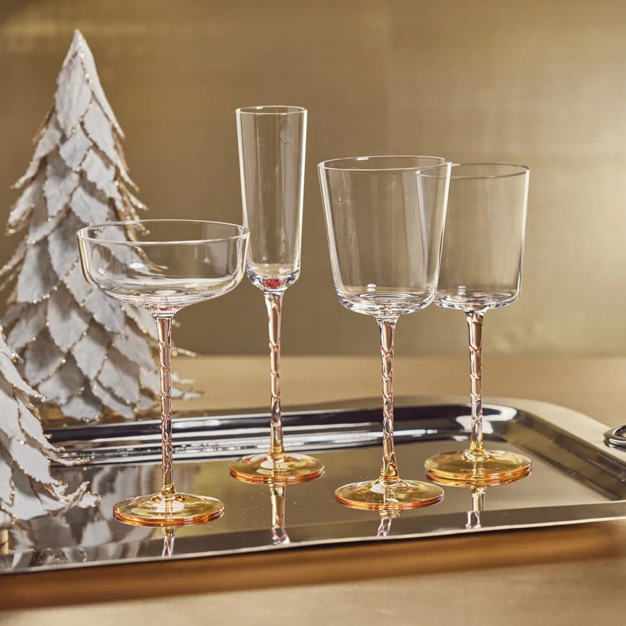 A set of four elegant VICENZA GLASSWARE RED WINE GLASSES by ZODAX, each with a capacity of 400 ml and intricate gold stems, are displayed on a silver tray. The background features a festive, white and gold decorative tree, creating a sophisticated holiday ambiance.