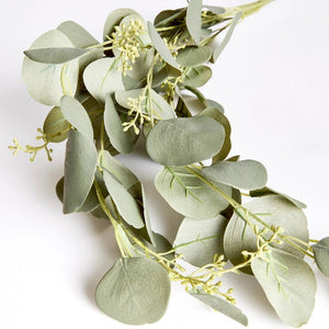 An arrangement of NAPA HOME AND GARDEN's SILVER DOLLAR EUCALYPTUS SPILLER, featuring round, green leaves with small yellowish buds, is set against a plain white background. The matte-textured leaves and slender, light green stems contribute to a refreshing greenery garland touch.