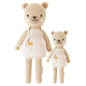 Two beige, hand-knit Goldie the Honey Bears from CUDDLE & KIND, one larger at 20 inches and one smaller, are standing side by side. Both bears are wearing white aprons that cross at the back. Made from safe, non-toxic materials, these fair trade dolls have simple features with no visible faces or distinguishing characteristics.