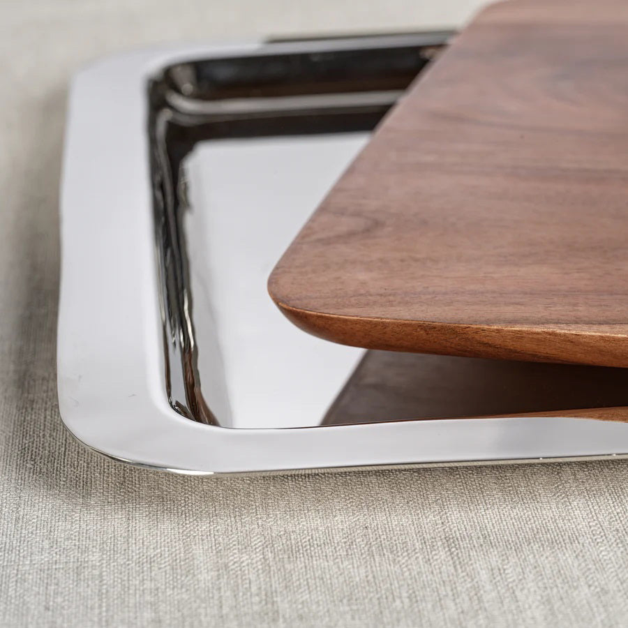 The BRASSERIE STEEL & ACACIA FUSION BOARD by ZODAX rests on a beige surface, boasting a modern design that melds warm acacia wood with sleek steel accents. It features polished, reflective metal handles and offers impressive dimensions for versatile use.