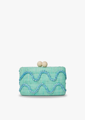 The KAYU Tierra Clutch is a small, rectangular raffia clutch with a turquoise woven texture, light blue wavy embroidery on a plain white background, and hand embroidery. It features two round wooden ball clasps on top.