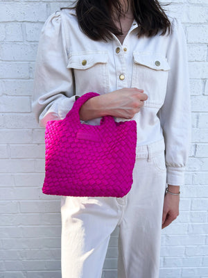 A woman with long brown hair, in a sleeveless cream knit top and blue jeans, holds a PARKER AND HYDE - MINI WOVEN TOTE BAG. The hand-woven tote by PARKER & HYDE features a subtle checkered pattern with light blue accents.