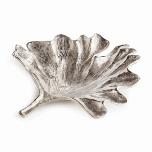 The FOLIA DECORATIVE SILVER TRAY by NAPA HOME AND GARDEN is a detailed, leaf-shaped piece expertly crafted through sand casting to highlight the natural intricacies of a leaf. This sophisticated aluminum tray features a polished finish and stands on three small legs, elegantly displayed on a white surface.