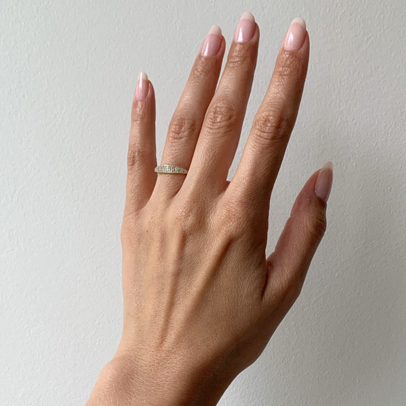 A hand with neatly manicured nails wears a diamond-studded ring on the ring finger, held against a plain white background.