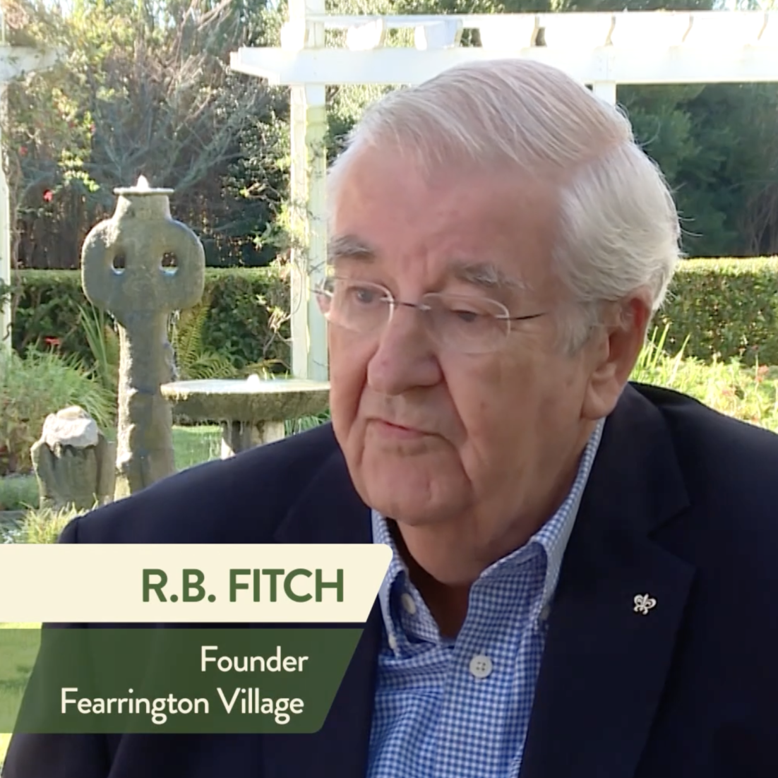 An older man wearing glasses and a navy blazer sits outdoors near a stone fountain. Text on the image reads: "R.B. Fitch, Founder, Fearrington Village." Trees and greenery are visible in the background.