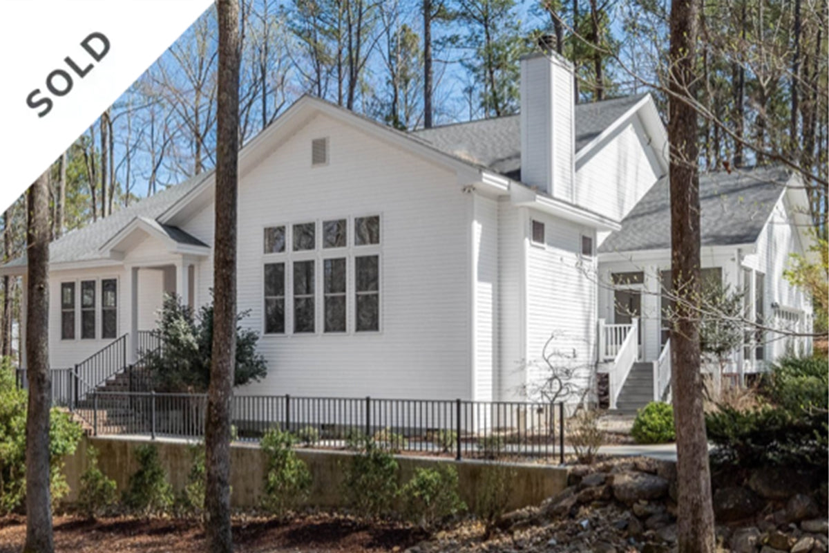 A modern white house with large windows, a chimney, and a front porch is surrounded by trees. A “SOLD” banner appears in the top left corner of the image.