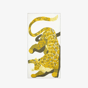 A woman with long, grey hair is wearing a white, loose-fitting dress and has an INOUI EDITIONS - NEOFELIS cotton and silk scarf from INOUI, featuring a snake pattern in yellow, draped around her shoulders. She stands against a plain, white background, looking directly at the camera.