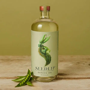 A clear glass bottle of SEEDLIP - GARDEN 108 NON ALCOHOLIC SPIRIT from SEEDLIP DRINKS against a white background. The bottle features a green label with an artistic illustration of peas and leaves forming a surreal face. It is crafted from botanical distillates and topped with a wooden cork adorned with a green ribbon.