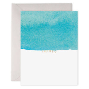 An E. FRANCES - DREAM BIG CARD by E.FRANCES PAPER, made from luxe heavyweight paper, featuring an original watercolor painting with a vibrant turquoise-blue gradient at the top and a white bottom, with "DREAM BIG" written in gold uppercase letters in the center, accompanied by an envelope placed behind it.