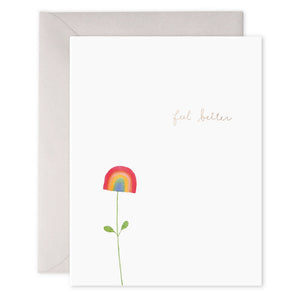 The E. FRANCES - RAINBOW FLOWER FEEL BETTER CARD by E. FRANCES PAPER is an elegantly simple greeting card with a plain white background, adorned with a hand-drawn rainbow flower featuring a green stem and leaves. The words "feel better" are written in small, delicate gold letters near the top right corner. Radiating positive energy, this card comes complete with an envelope.
