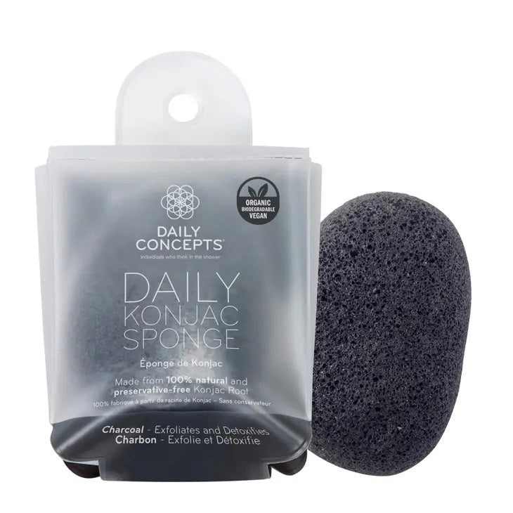 A black Daily Concepts Charcoal Konjac Sponge is placed beside its packaging, labeled &quot;Daily Concepts Daily Konjac Sponge.&quot; The packaging highlights that it is made from 100% natural and preservative-free konjac root and features the word &quot;charcoal.&quot; It is organic, vegan, biodegradable, and highly effective for removing skin impurities.