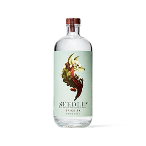 A clear glass bottle of SEEDLIP - SPICE 94 NON ALCOHOLIC SPIRIT by SEEDLIP DRINKS is shown against a white background. The bottle features a brown cap and a light green label adorned with an artistic illustration of various spices and herbs. The text on the label reads "Seedlip Spice 94 Aromatic botanical distillates.