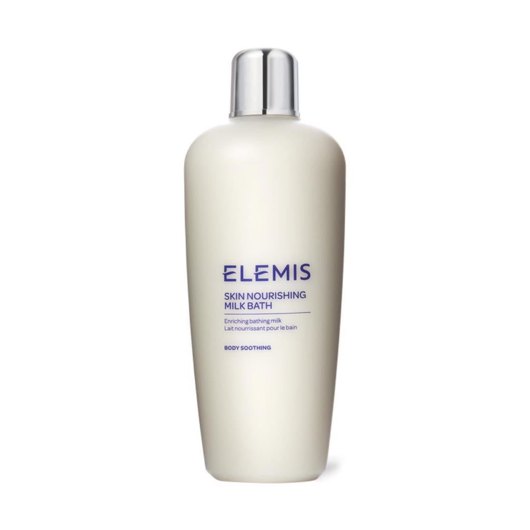 A white, cylindrical bottle of ELEMIS - SKIN NOURISHING MILK BATH with a silver cap features blue text on the label that includes phrases like &quot;Body Soothing&quot; and &quot;Emollient bath milk,&quot; emphasizing its purpose as a nourishing bath milk for excessively dry skin.