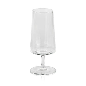 The ZODAX FLUTED TEXTURED COCKTAIL GLASS is a pristine, empty glass with a refined, tall and narrow cylindrical design and a sturdy, flat base. Measuring approximately 3 inches in diameter and 7 inches in height, this glass features a clear and transparent body that beautifully reflects light on its textured surface. The short stem seamlessly connects the base to the main body.