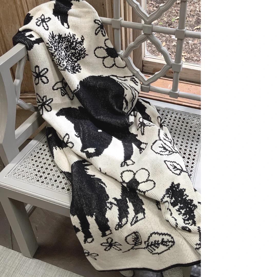 Presenting the FEARRINGTON SIGNATURE COLLECTION - BELTIE BARNYARD KNIT THROW by CALHOUN &amp; CO., this cylindrical knitted item showcases a black and white design with a close-up of a rabbit holding a flower. Made in America, it features minimal detailing that emphasizes contrasting shades, creating a simple and stylized depiction of the rabbit and flower.