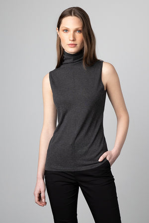 A woman with long, straight hair is standing against a plain gray background. She is wearing a sleeveless seamed funnel top from KINROSS CASHMERE and black cashmere pants. Her left hand is in her pocket, and she is looking directly at the camera with a neutral expression.