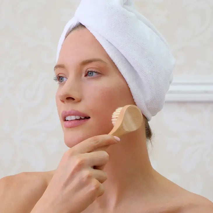 In front of its packaging, the Wooden-handled FACIAL DRY BRUSH displays a photo of the brush, the brand name &quot;DAILY CONCEPTS,&quot; and text highlighting features such as &quot;Daily Facial Dry Brush&quot; and &quot;For Radiant Looking Skin.&quot; This exfoliating tool, which is perfect for lymphatic drainage, also boasts a Vegan logo on the top right.