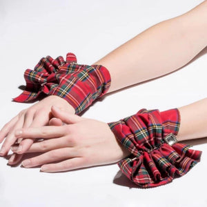 A pair of CATHERINE OSTI Wallace Cuffs in red, featuring elegant plaid fabric with red, black, and yellow Scottish tartan patterns. Each cuff is gathered in the middle with a small square rhinestone embellishment, creating a ruffled effect on both sides. The cuffs are displayed against a plain white background.