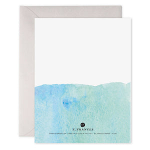 An E. FRANCES - DREAM BIG CARD by E.FRANCES PAPER, made from luxe heavyweight paper, featuring an original watercolor painting with a vibrant turquoise-blue gradient at the top and a white bottom, with "DREAM BIG" written in gold uppercase letters in the center, accompanied by an envelope placed behind it.