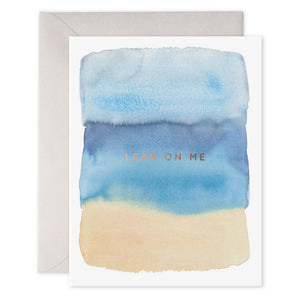 The E. FRANCES - LEAN ON ME CARD by E.FRANCES PAPER showcases a serene scene with a watercolor design in shades of blue and beige. The words "LEAN ON ME" are elegantly printed in gold foil at the center on heavyweight paper, accompanied by a plain light gray envelope.