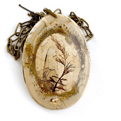 The NECKLACE SALINAS RESIN XL PENDANT LONG CHAIN by PELLINI showcases an exquisite oval-shaped pendant reminiscent of Donatella Pellini jewelry. This pendant encapsulates a preserved plant and an insect wing within a resin-like material, suspended from an intricate, antique-style bronze chain. The slightly faded natural elements enhance its vintage charm.