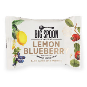 A white packet of Big Spoon Roasters Lemon Blueberry Cashew Snack Bar features colorful illustrations of lemons, blueberries, and cashews on the front. The packaging indicates that it is vegan, dairy-free, gluten-free, soy-free, and palm oil-free, with a net weight of 60g (2.12 oz).