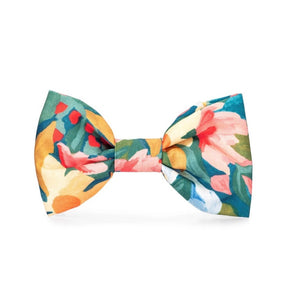 The DOG BOW TIE (STANDARD, WILDFLOWER) from THE FOGGY DOG boasts a vibrant floral print in shades of green, yellow, pink, red, and white. This impeccably tied bow tie stands out against a plain white background, making it an ideal choice for those who value handcrafted pet products.