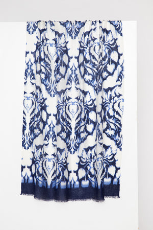 The KINROSS CASHMERE - MEDALLION PRINT SCARF by KINROSS hangs against a plain white background. This luxurious scarf showcases an intricate blue and white floral and scroll medallion pattern with a gradient effect, transitioning from dark blue at the bottom to lighter shades toward the top. The edges are delicately frayed.